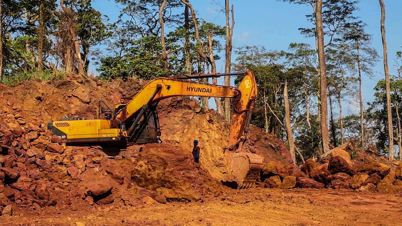 Excavator cutting into red earth beside forest at a mining site in Ghana